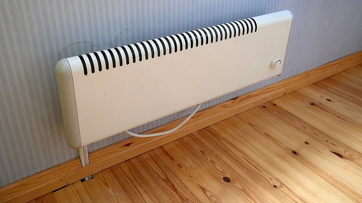 Hvit elektrisk panelovn montert på veggen like over gulvlisten